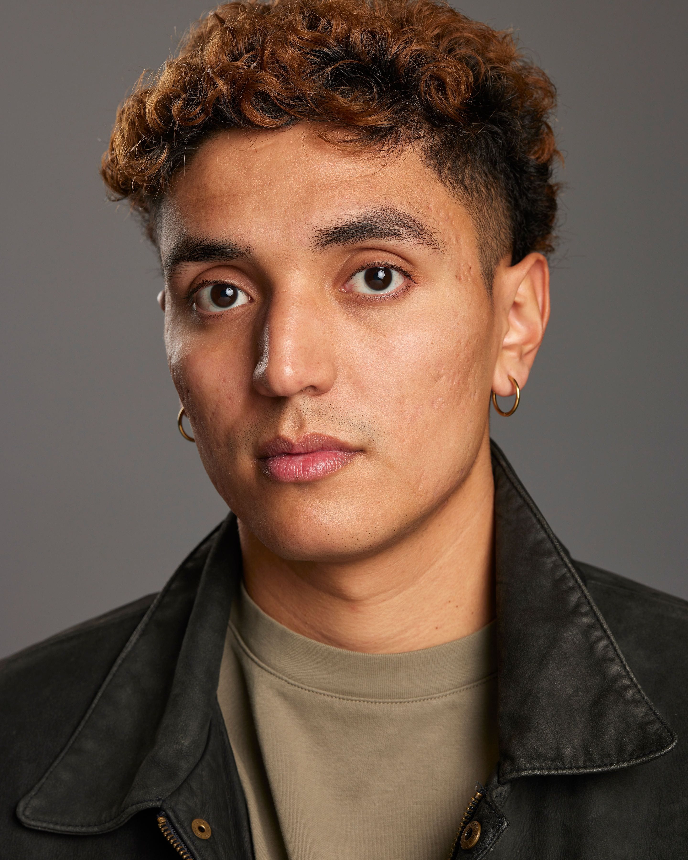 José Alfredo Alvarez in a leather jacket and olive shirt against a gray studio background.