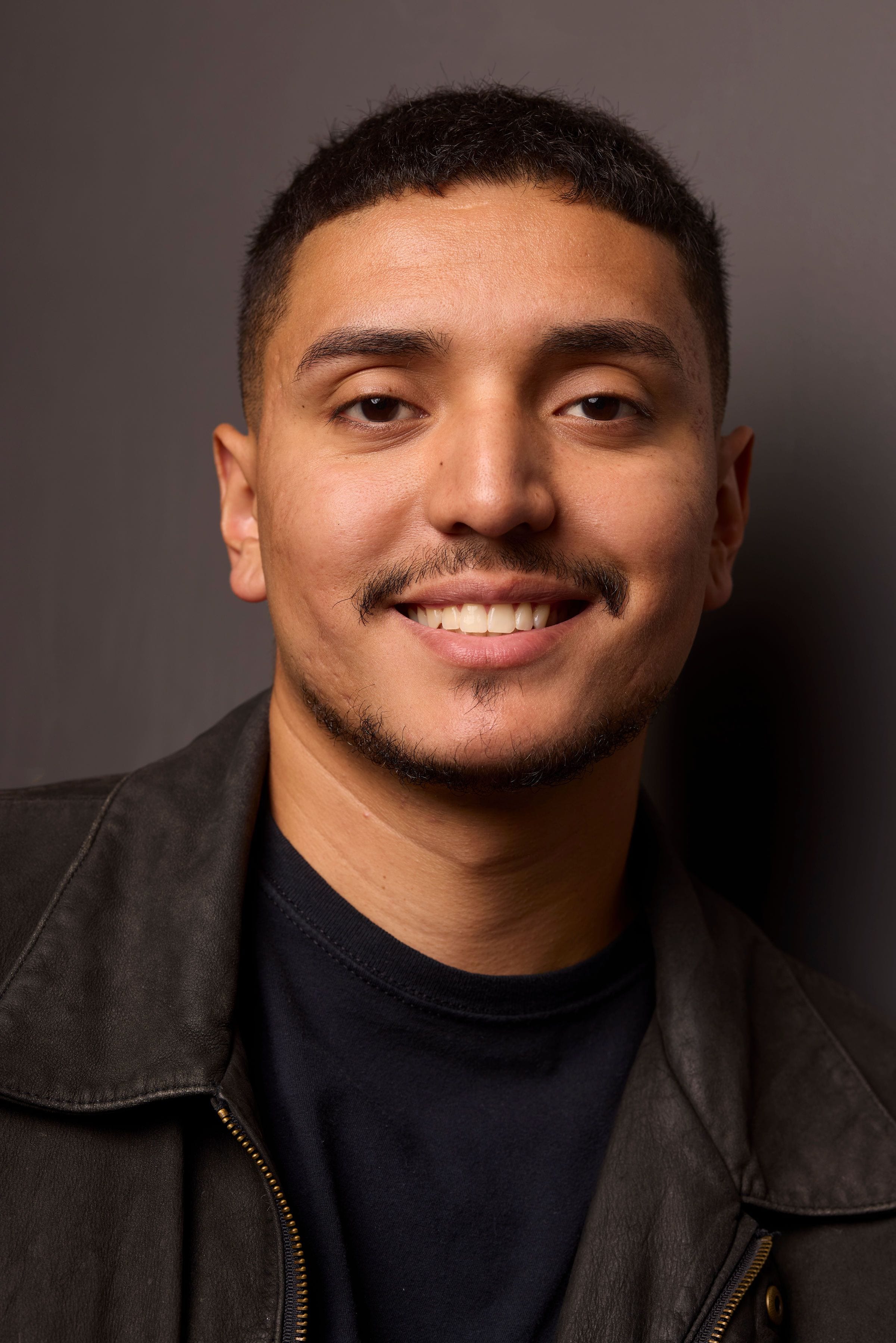 José Alfredo Alvarez smiling in a black leather jacket against a dark background.